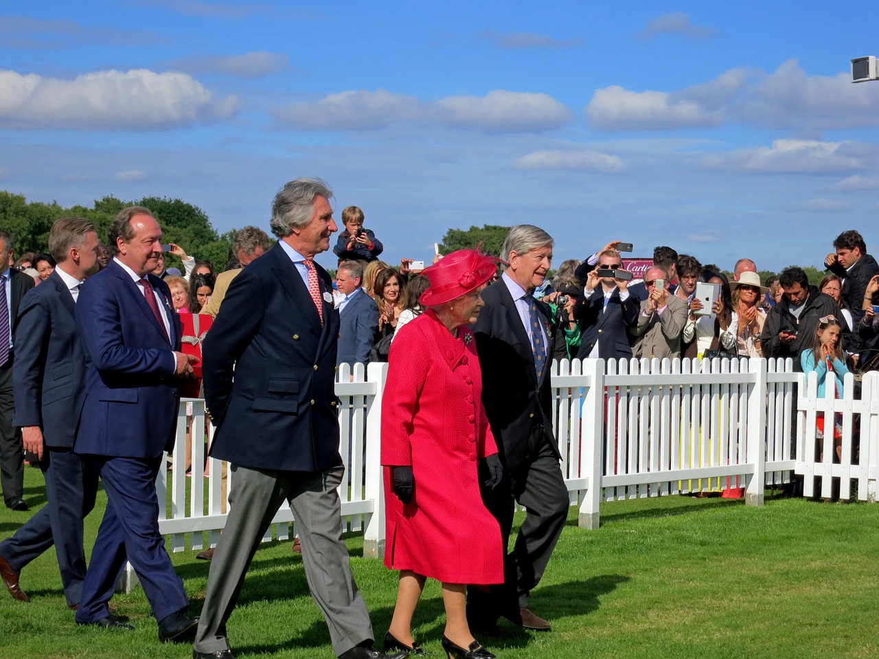 Queen Elizabeth II walks with a group of people and dogs.