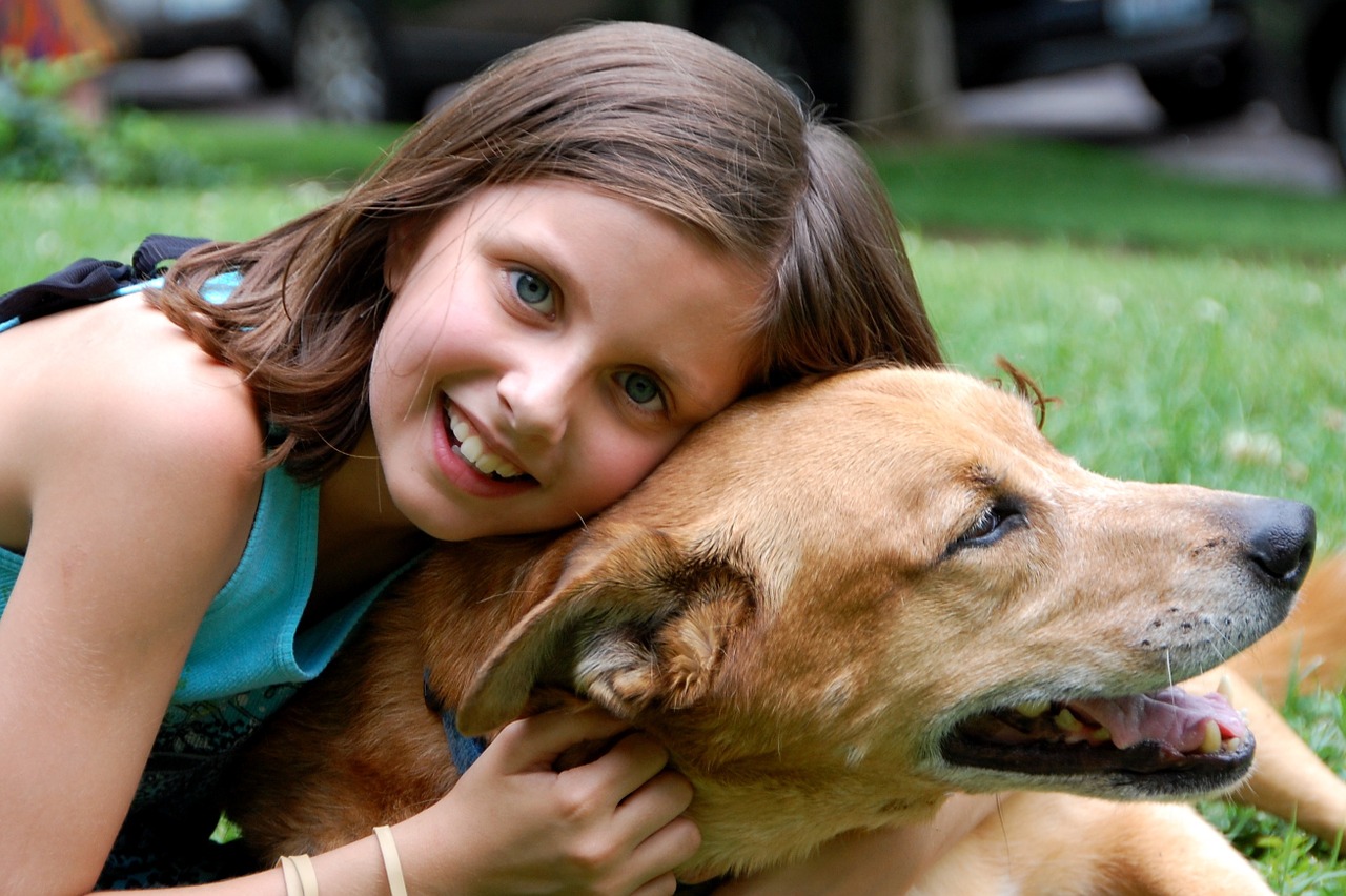 A girl laying on the grass with a dog.